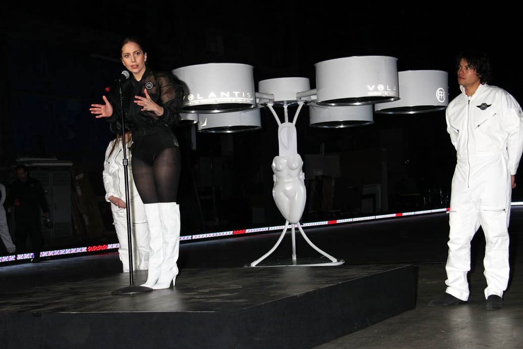 Lady Gaga speaking at a press conference with her flying dress behind her