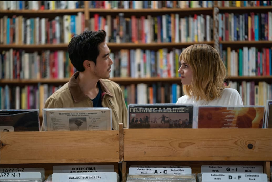 Lucy Boyton and Justin Min look at each other in a record shop in a still from 'The Greatest Hits'