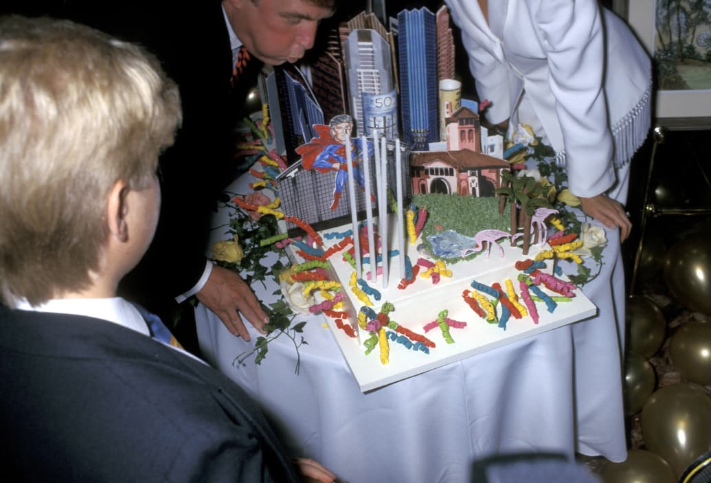 Donald Trump blows out the candles of his birthday cake at his 50th birthday party, which included an early example of him likened to Superman.