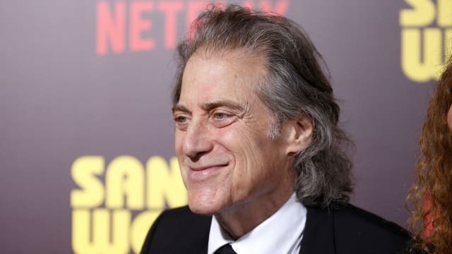 Richard Lewis, wearing a suit and tie, poses at a premier.