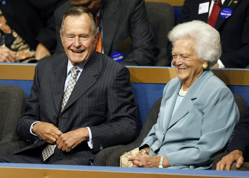 George H. W. Bush and his wife, Barbara Bush, laugh together while seated.