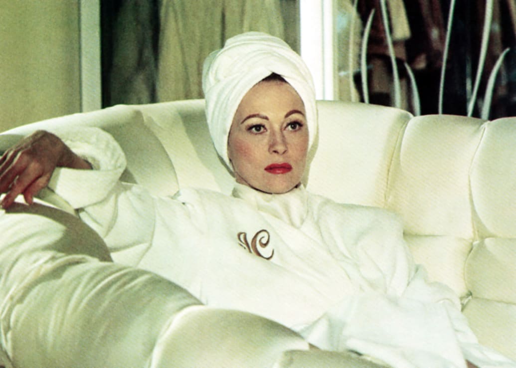 Faye Dunaway sits on a couch in a still from ‘Mommie Dearest’
