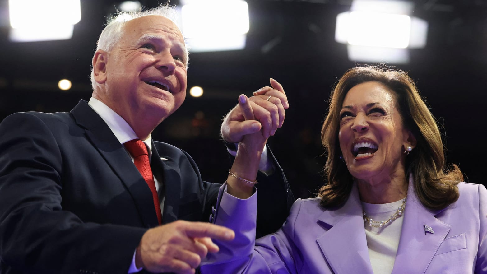 Kamala Harris and Tim Walz smile while embracing each other at an event.