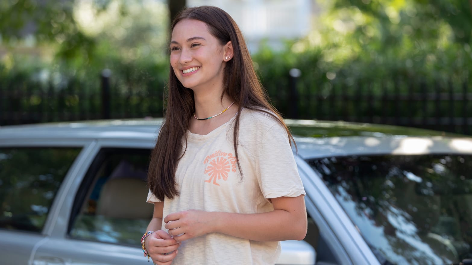 A girl with long brown hair and a white T-shirt smiles.