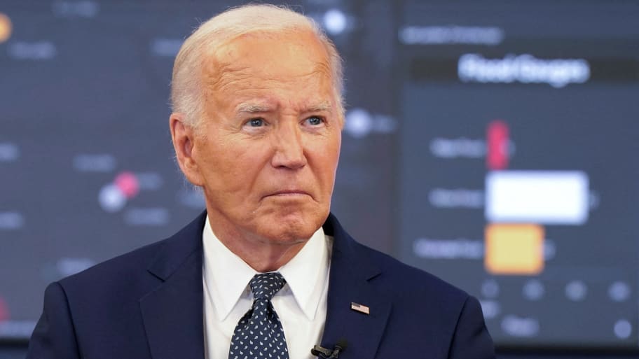 Joe Biden, wearing a suit and microphone, stares forward. 