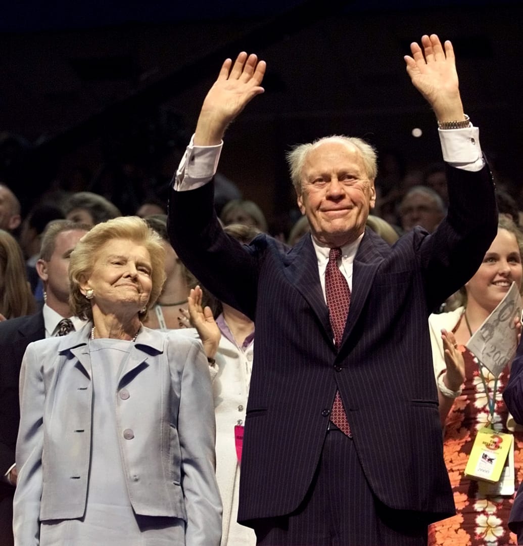 Gerald R. Ford raises his hands while standing next to his wife. 