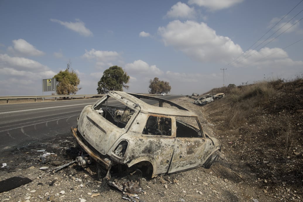 A photo including a destroyed car on the road side in Kfar Aza, Israel