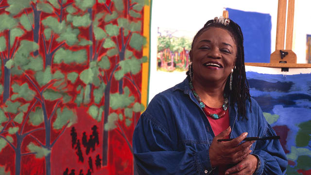 Portrait of American artist Faith Ringgold as she poses in front of one of her paintings, 1999.