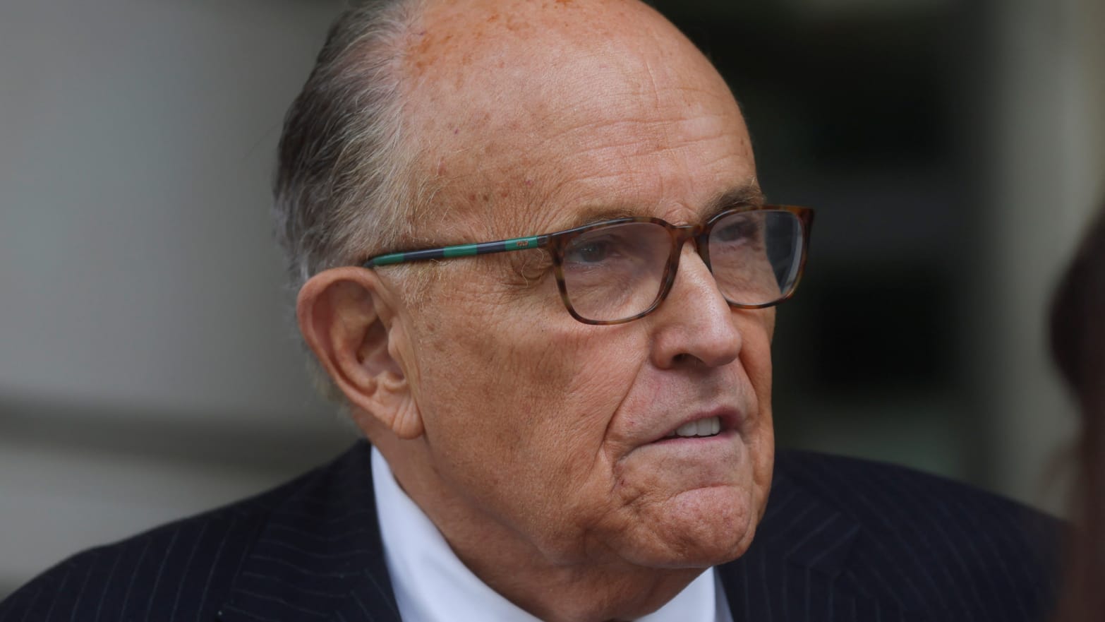 Rudy Giuliani, wearing glasses and a suit, looks forward as he leaves a federal courthouse.