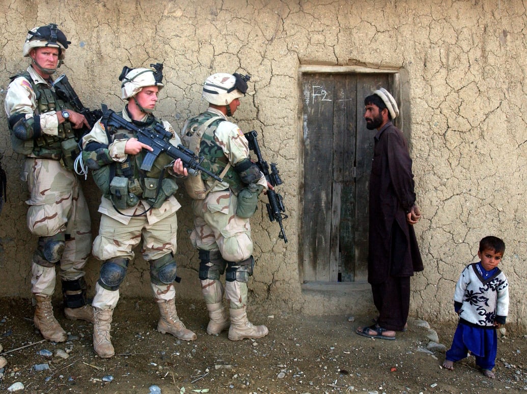 A picture of an Afghan man and his son looking at American soldiers who are outside of their home.