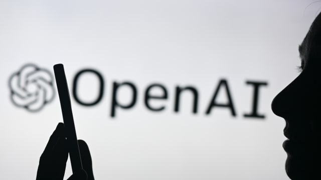An image of a woman holding a cell phone in front of the Open AI logo displayed on a computer screen, on April 29, 2024, in Edmonton, Canada.