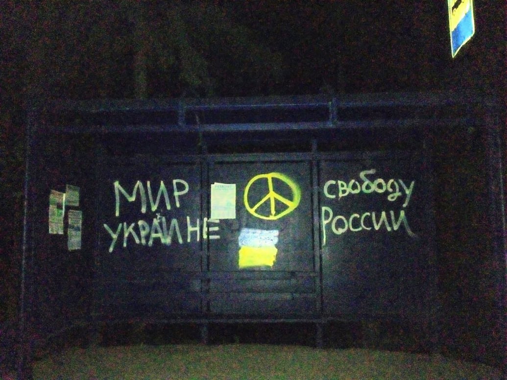Yellow spray paint “Peace to Ukraine, Freedom to Russia” with a peace sign on a bus stop shelter.