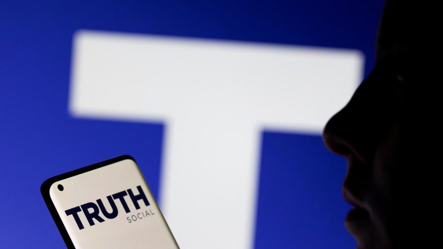 The Truth social network logo displayed behind a woman holding a smartphone.