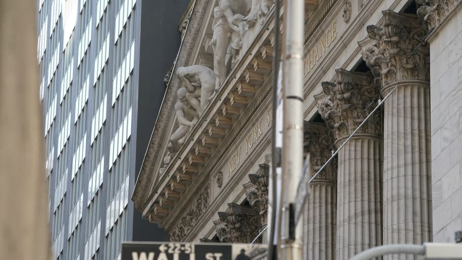 The exterior of the New York Stock Exchange (NYSE) in New York with a Wall St. sign in front of it.