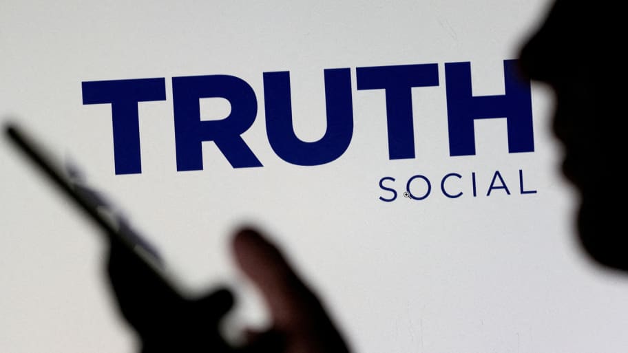 The Truth social network logo is seen displayed behind a woman holding a smartphone in a picture illustration.