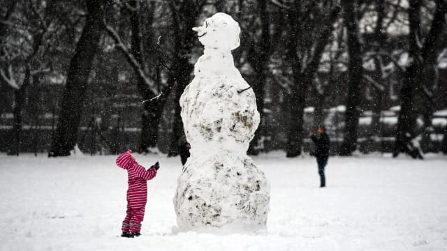 A child looks at a giant snowman as they stand in a snow-covered Victoria Park in Glasgow on February 9, 2021.