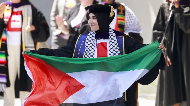 Graduate Malak Afaneh waves a Palestinian flag as she crosses the stage to receive her degree during the UC Berkeley Law School commencement at the Greek Theater in Berkeley Friday, May 10, 2024.