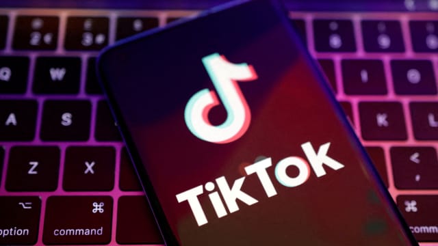 A TikTok logo is displayed on a phone screen, which is sitting on top of a laptop’s keyboard.