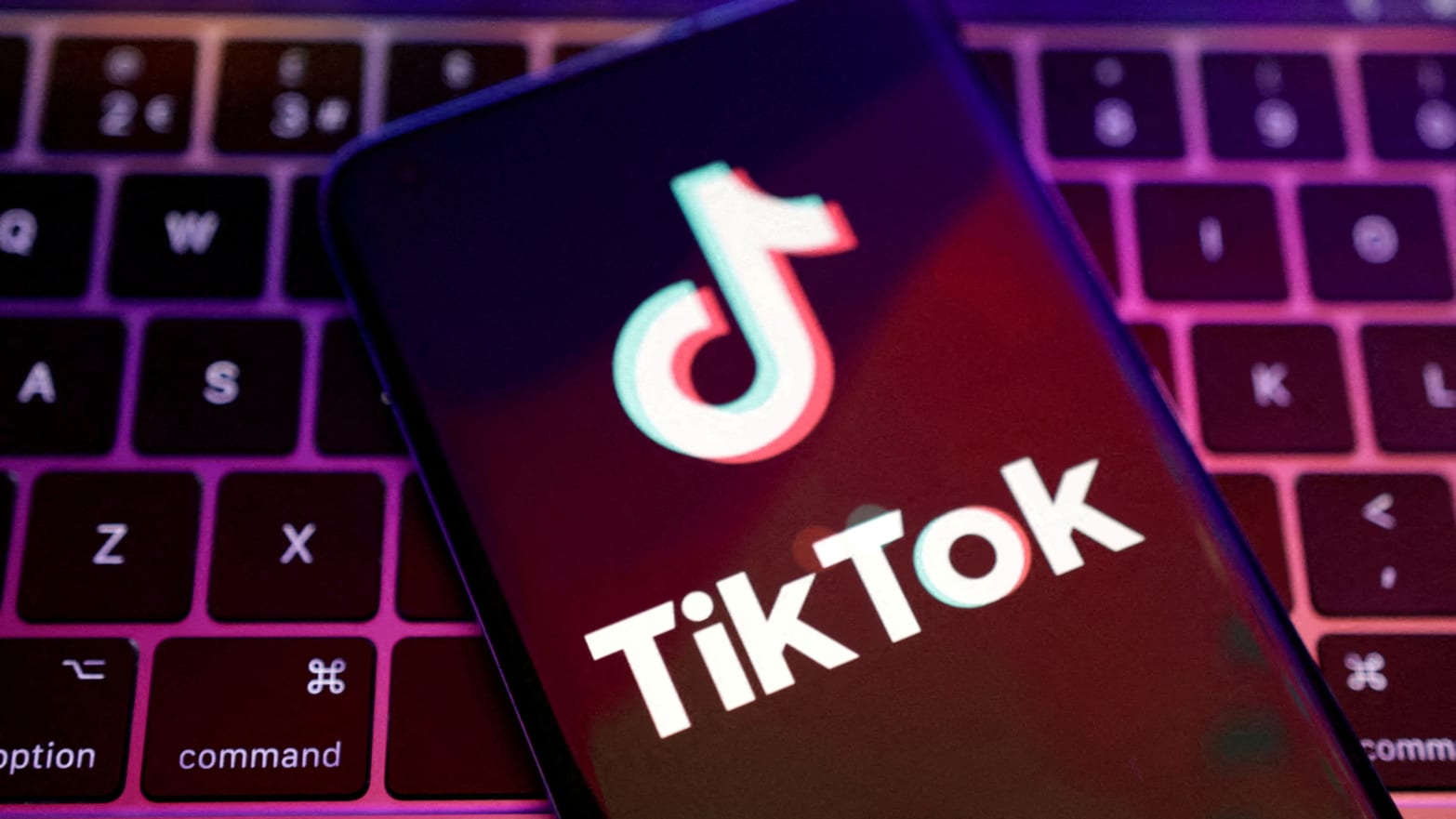 TikTok logo is on a phone placed over a laptop keyboard.