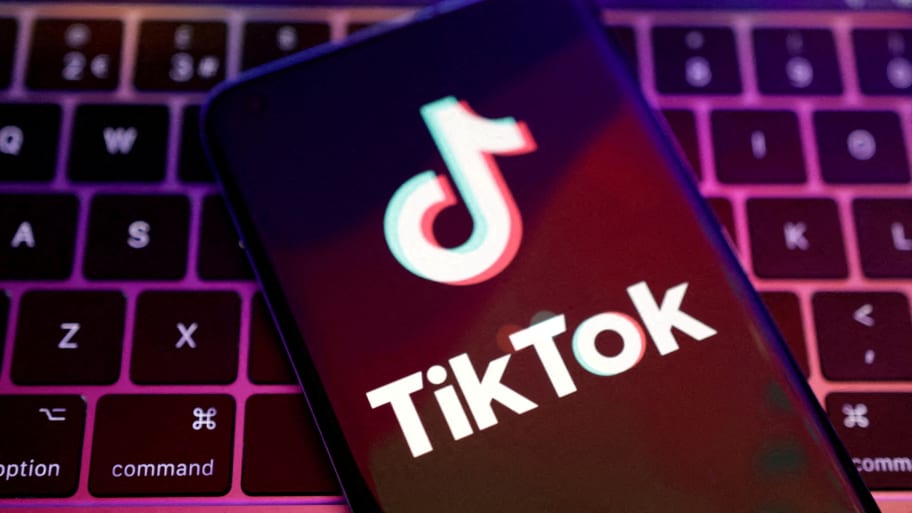 The TikTok logo on a phone screen, with a laptop keyboard in the background.