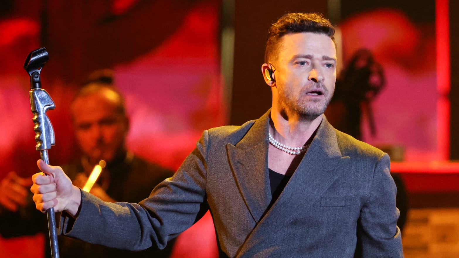 Justin Timberlake holds a microphone stand while performing on stage.