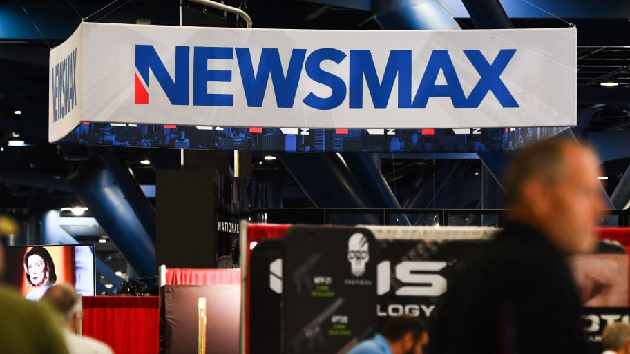 Signage for the Newsmax conservative television broadcasting network is displayed at a broadcast TV booth at the National Rifle Association