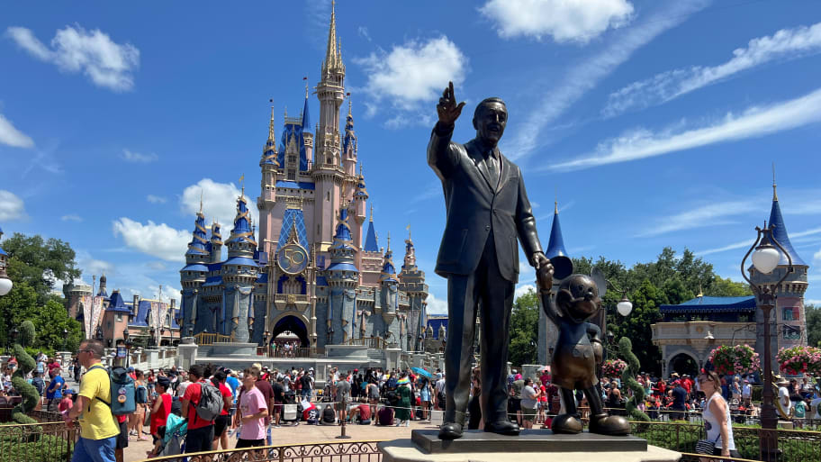 The entrance to Magic Kingdom at Walt Disney World, showing a statute of Walt Disney in the foreground and a castle in the background.