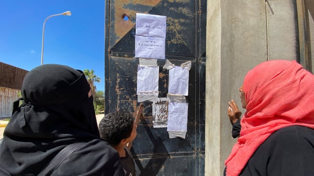 Two women and a boy look at missing people list in Libya following a flood.