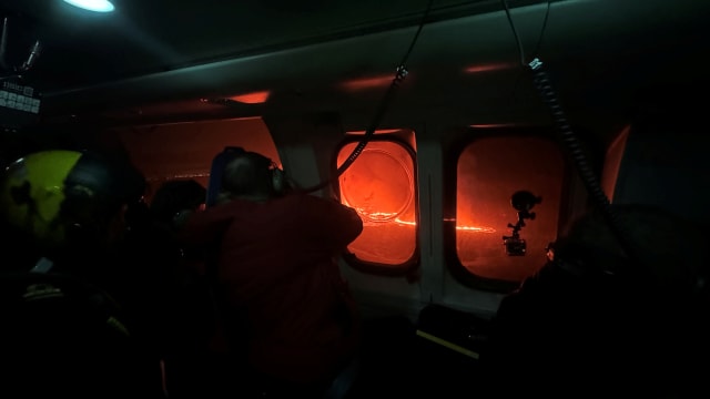 People look out of a coast guard helicopter at an erupting volcano in Iceland.