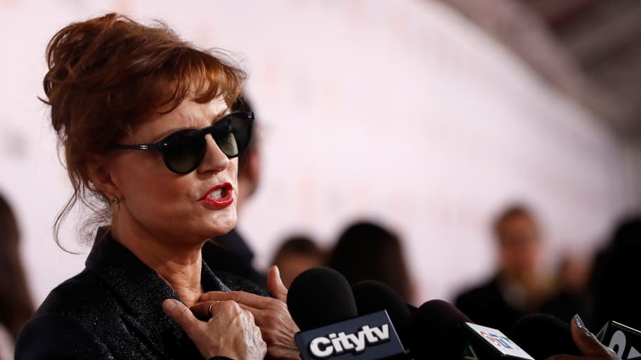 Susan Sarandon, wearing sunglasses, speaks into a microphone during an interview.