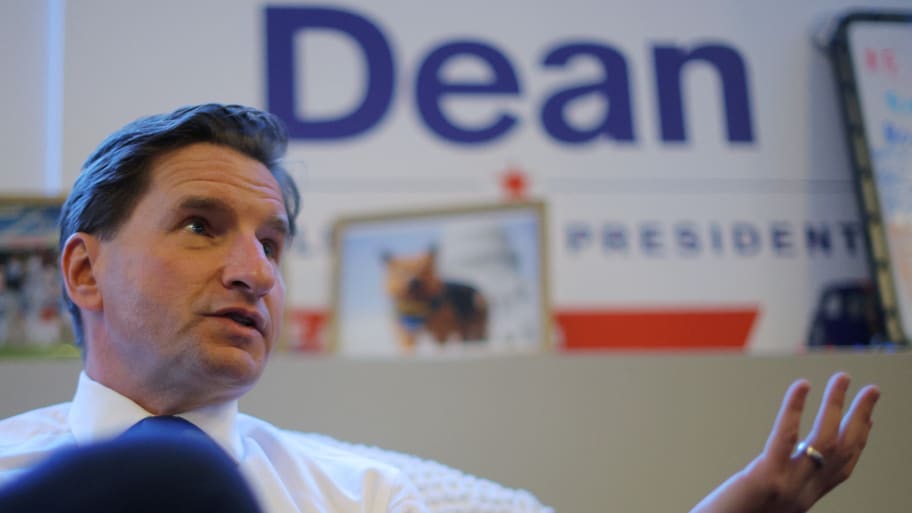 Dean Phillips, wearing a shirt and tie, speaks during an interview, with a “Dean For President” sign in the background.