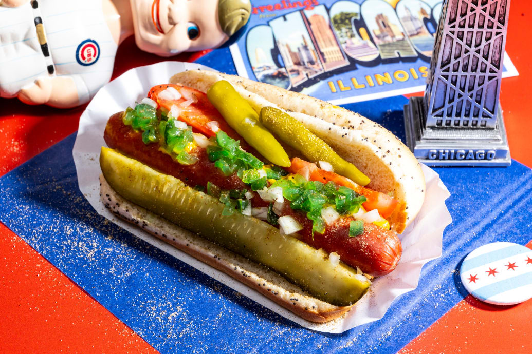A hot dog with pickles against a background of Chicago memorabilia including a Cobs bobblehead