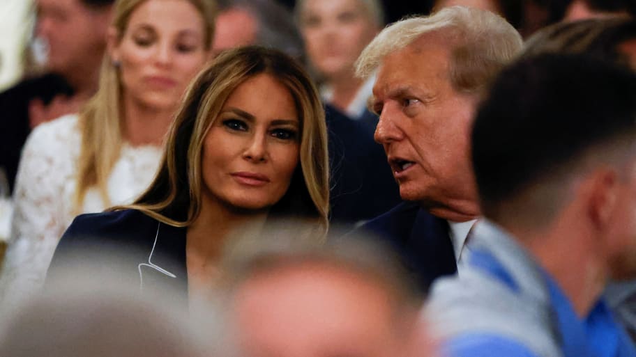 Melania Trump stares forward while Donald Trump faces her and speaks.