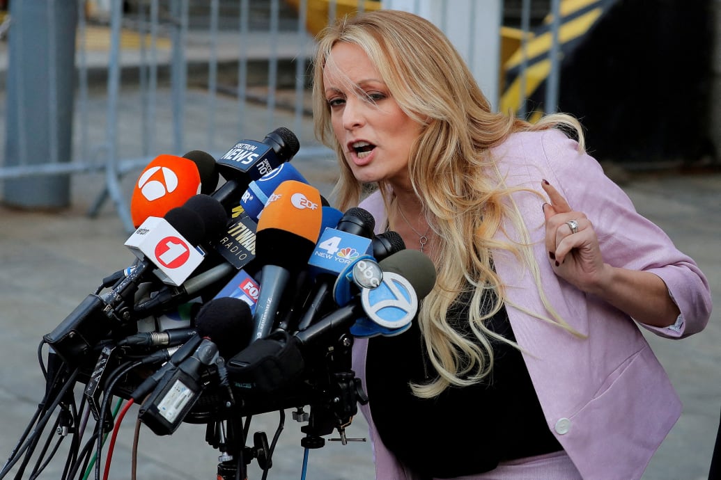 Stormy Daniels speaks into a podium filled with reporters’ microphones outside a courthouse.