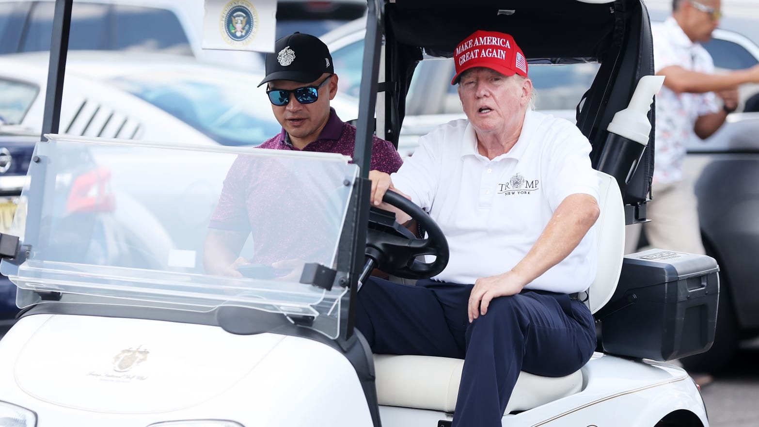 Former President Donald Trump drives a golf cart accompanied by aide Walt Nauta