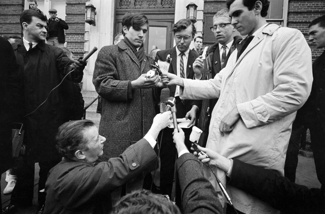 A photograph of reporters gathered near CNA pacifists as they burn their draft cards at a Vietnam War protest.