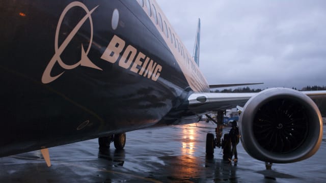 A Boeing jet sits on a runway with a cloudy sky in the background.
