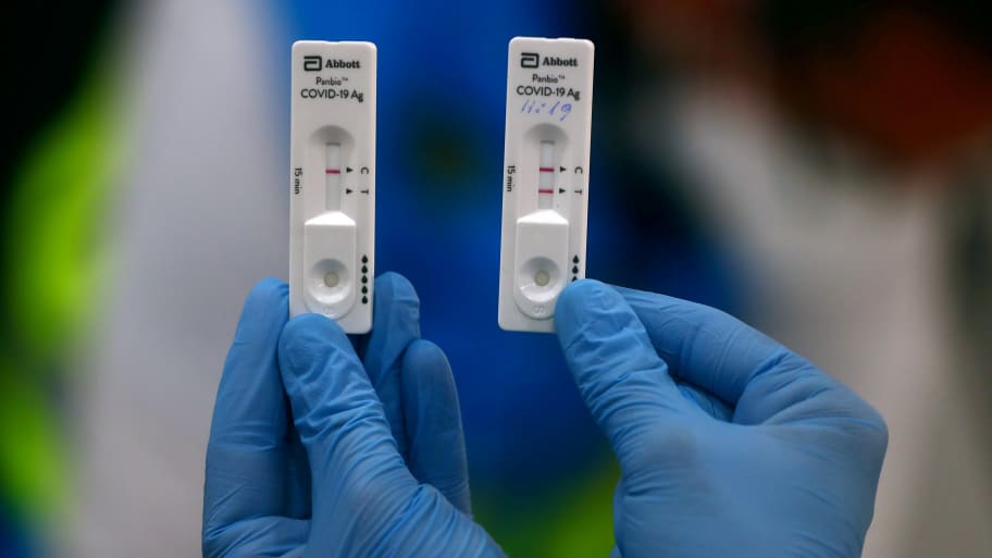 Two COVID tests are held in a gloved hand, one negative and one positive.