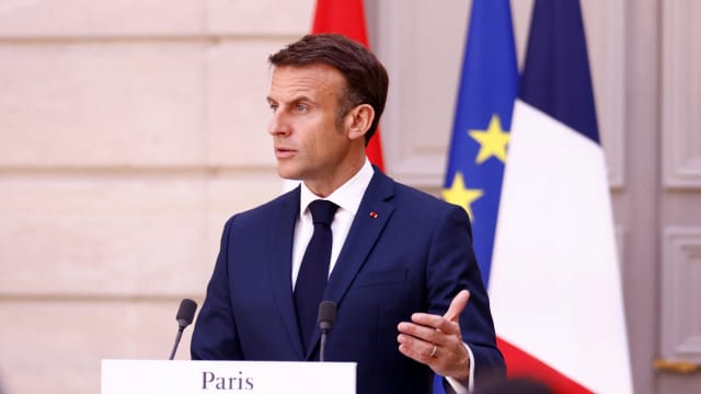 Emmanuel Macron speaks in front of flags at an event.