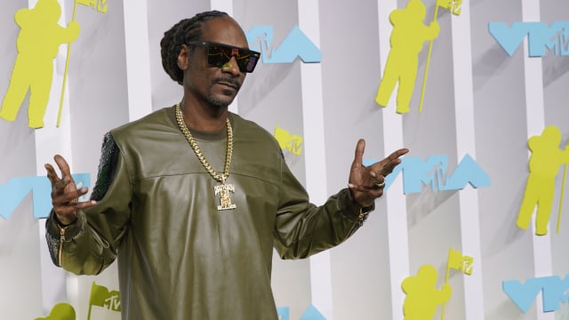 Snoop Dogg has his hands up while he poses for a photo outside an event.