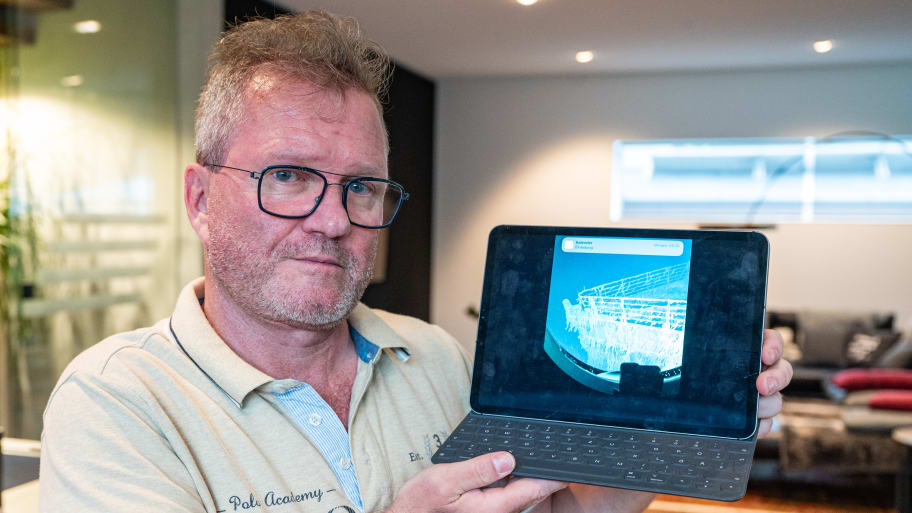 Arthur Loibl, a former passenger on the Titan, stands in his house with a tablet showing a photo of the Titanic.