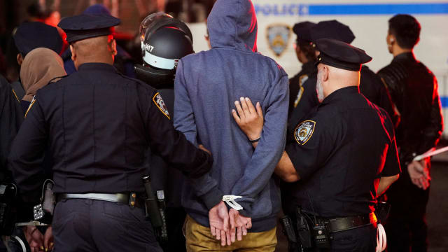 NYPD officers walk a detainee in handcuffs from a Columbia University protest.