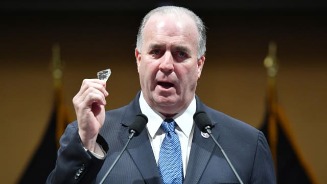 Dan Kildee holds up a shard of glass while speaking.