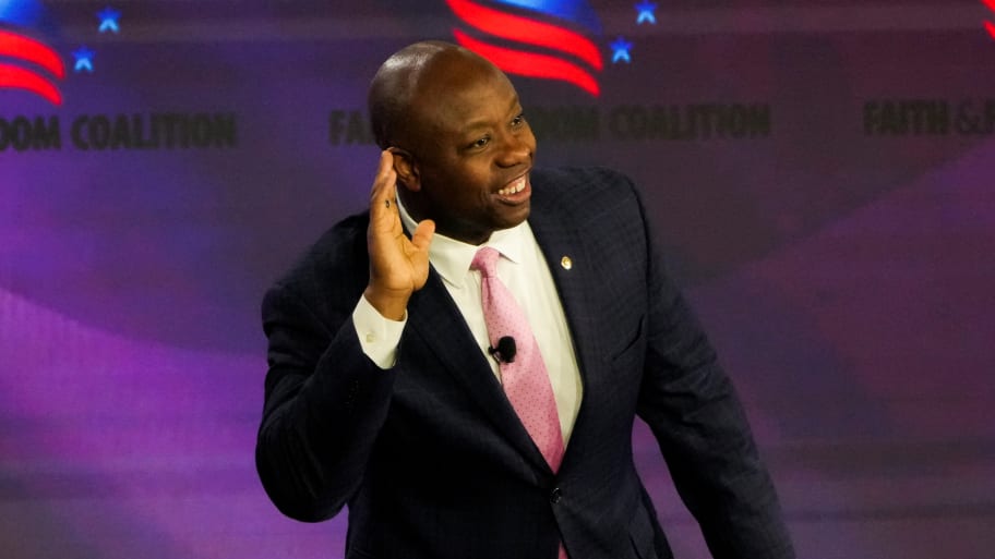 Tim Scott smiles with his hand to his ear during a conference.