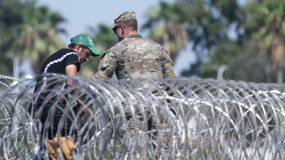 A member of the National Guard helps a migrant climb on top of a shipping container after he crossed the Rio Grande.