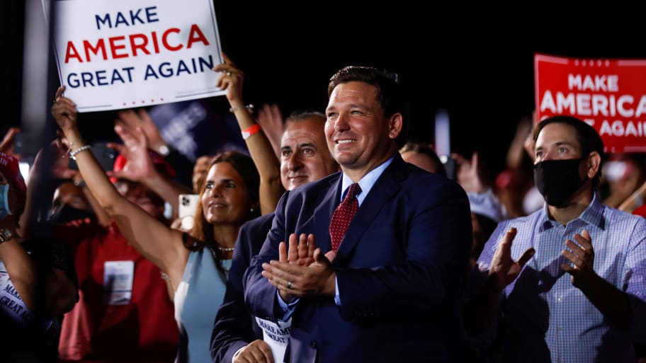 Ron DeSantis looks in awe at a Trump rally in front of a MAGA sign