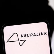 The Neuralink logo is displayed on a phone with a silhouette of Elon Musk in the background.