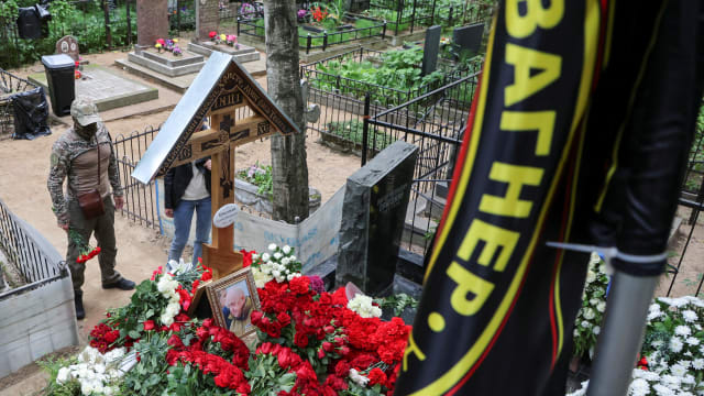 People stand in front of the grave of Russian mercenary chief Yevgeny Prigozhin, with a flag displaying the logo of Wagner private military group seen in the foreground, at the Porokhovskoye cemetery in St. Petersburg, Russia, Aug. 30, 2023. 