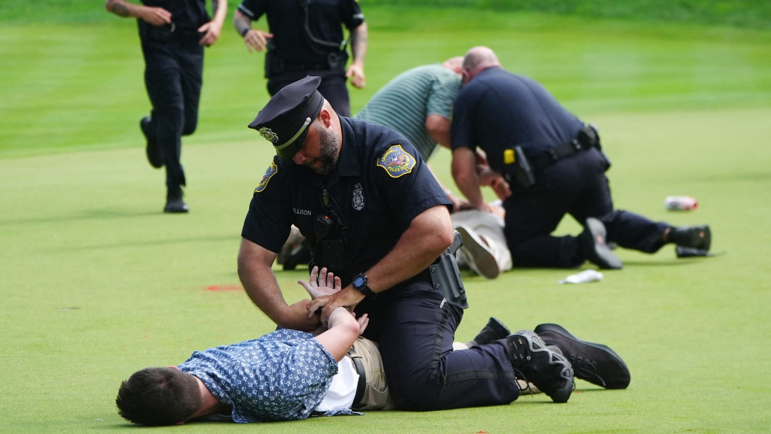 An officer handcuffs a prone protester who ran onto the 18th green of a PGA Tour event.