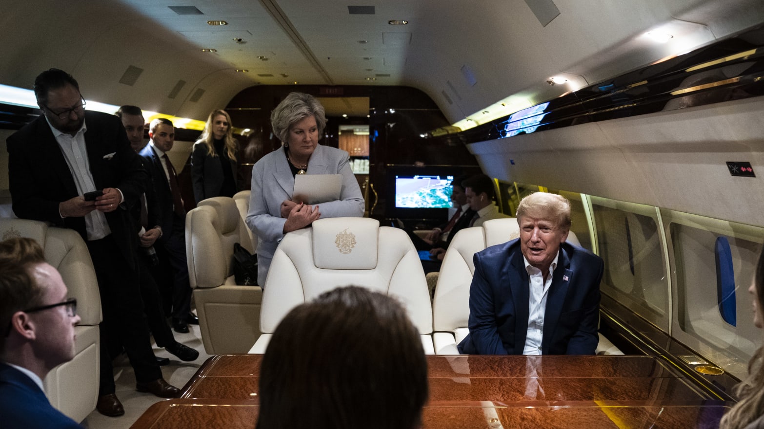 Former President Donald Trump speaks with Susie Wiles, center, staff and reporters while flying home on his airplane.